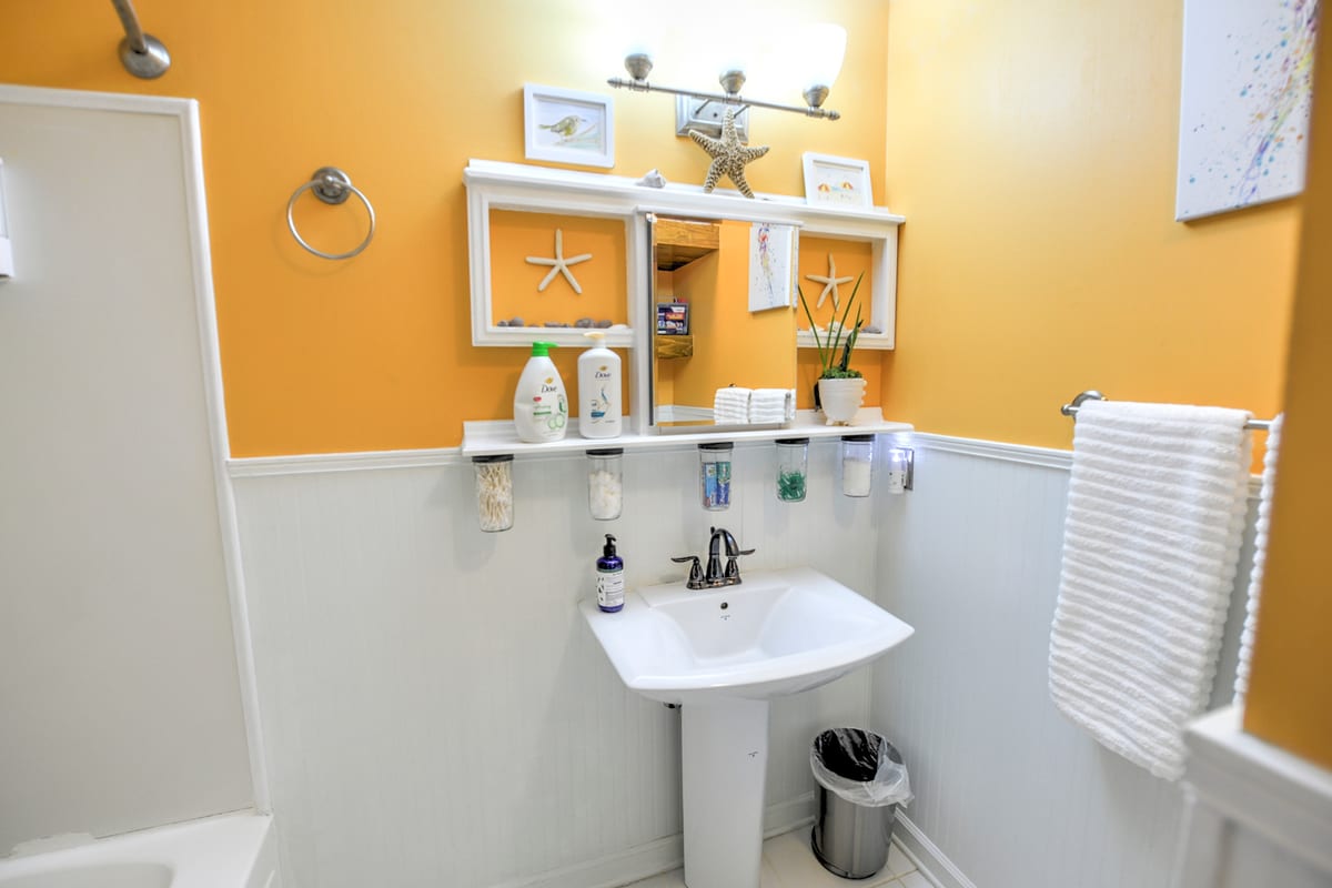 Bathroom with pedestal sink, beadboard walls, and coastal shelves