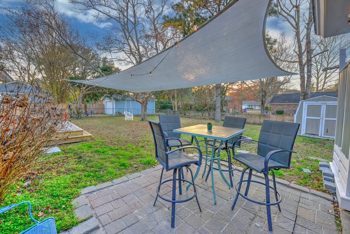 High-top patio table for four under a shade sail with string lights